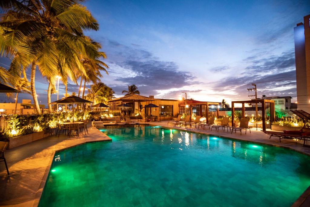 a pool with chairs and palm trees at night at Celi Hotel Aracaju in Aracaju