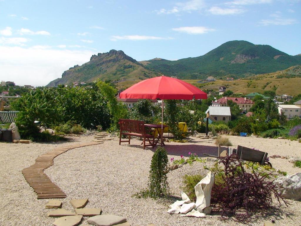 un patio con sombrilla roja, mesa y banco en Dom Pod Zvezdopadom Guest House, en Koktebel