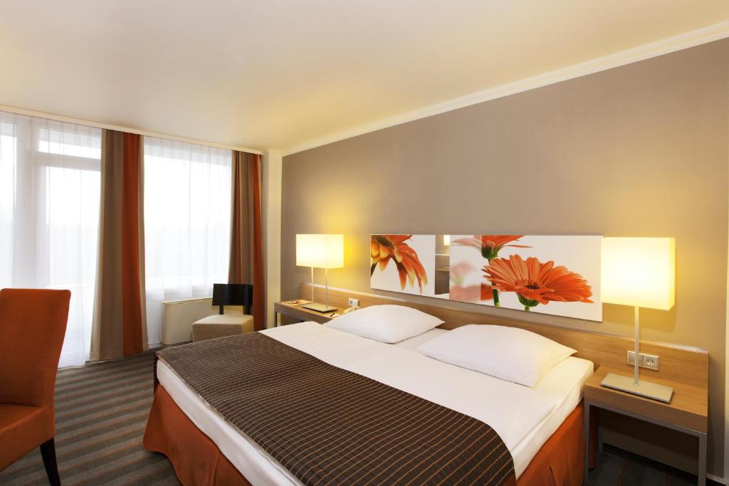 pokój hotelowy z dużym łóżkiem i 2 lampami w obiekcie H4 Hotel Frankfurt Messe w Frankfurcie nad Menem
