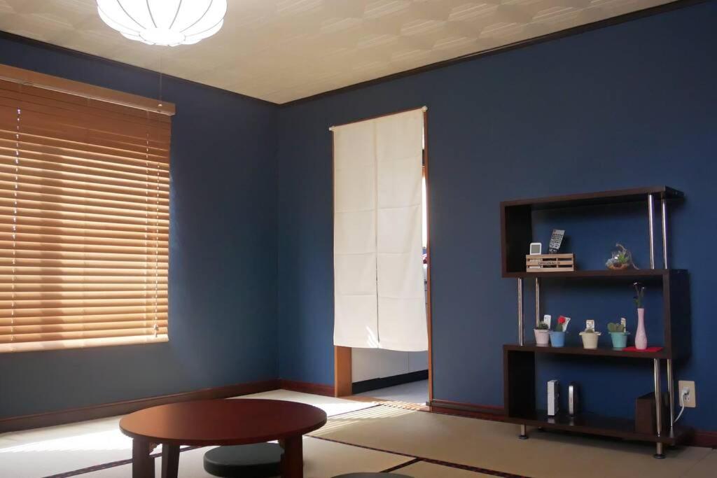 Zimmer mit einer blauen Wand mit einem Tisch und einem Stuhl in der Unterkunft 民泊 桔梗 in Awaji