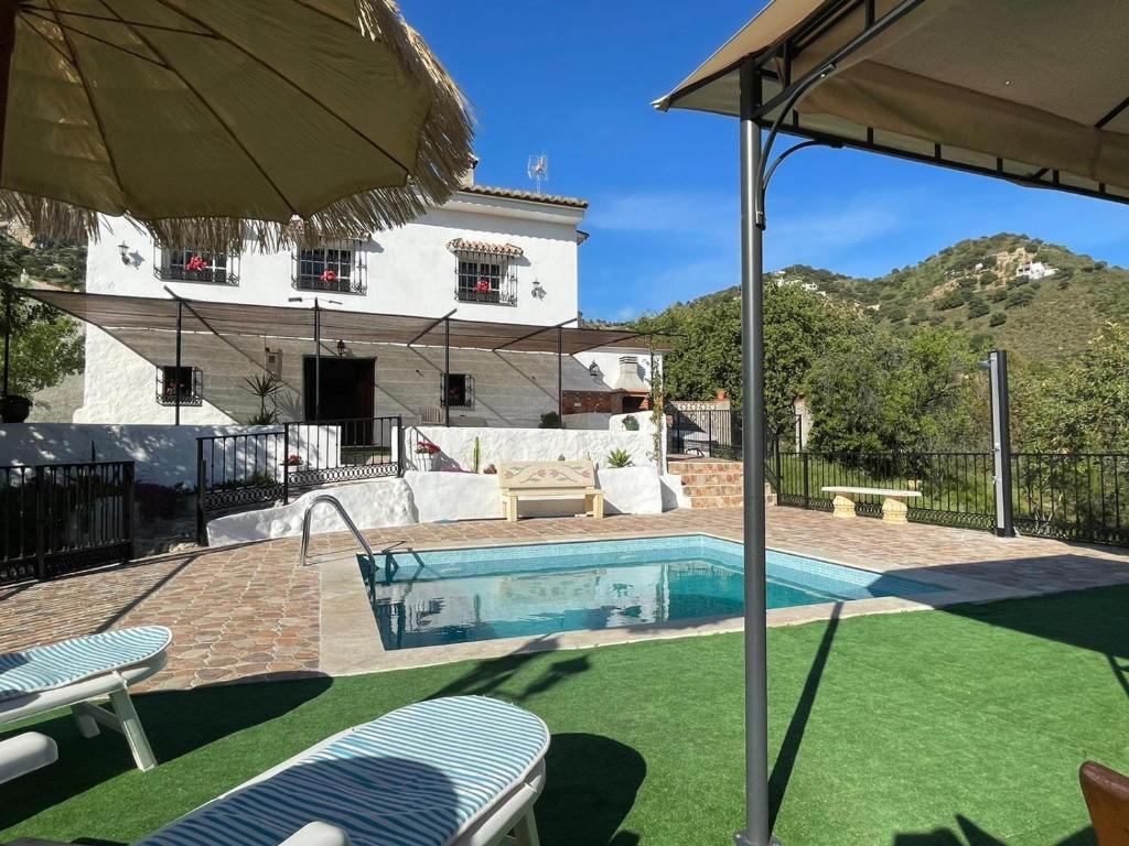 a swimming pool with an umbrella and a house at Alojamiento Rural El Paraíso del Chorro in El Chorro