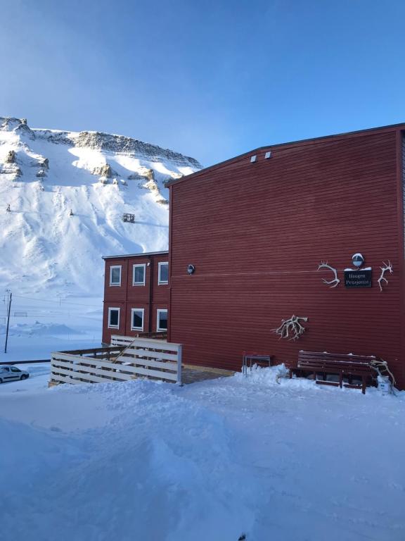 a red building with a snow covered mountain in the background at Haugen Pensjonat Svalbard in Longyearbyen