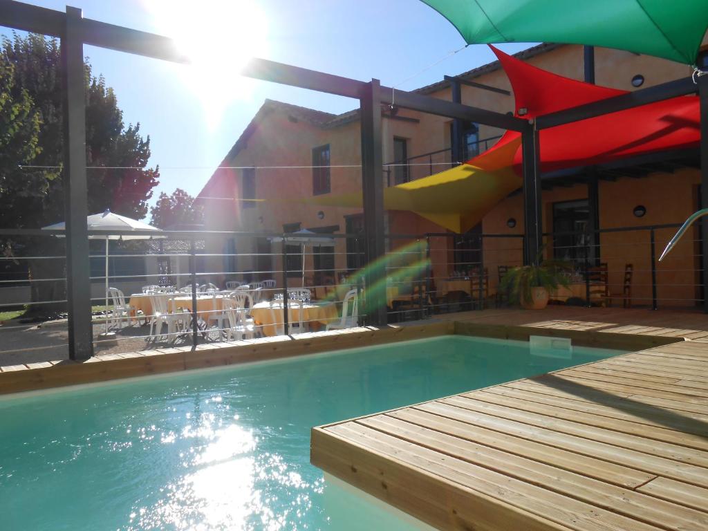 a swimming pool with a wooden deck and an umbrella at La Petite Ecole in Marciac