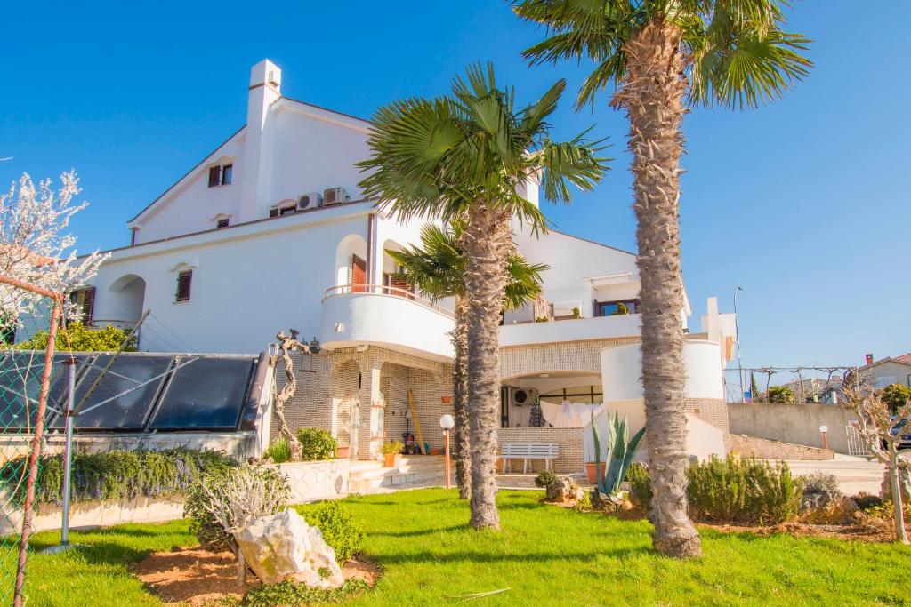 una grande casa bianca con palme di fronte di Apartments Punta & Vista in Krk a Krk