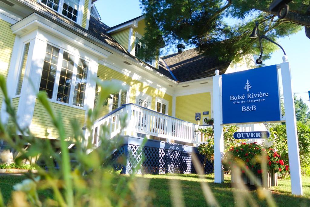 une maison avec un panneau bleu devant elle dans l'établissement Boisé Rivière, à Bolton-Est