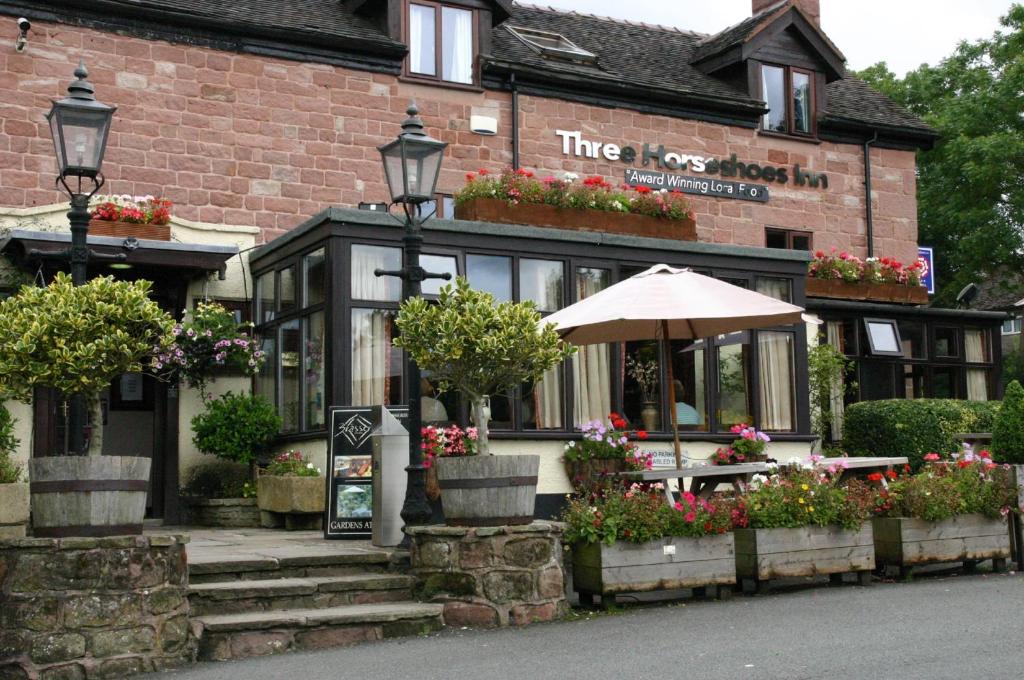 una posada con una mesa y una sombrilla delante de ella en Three Horseshoes Country Inn, en Leek