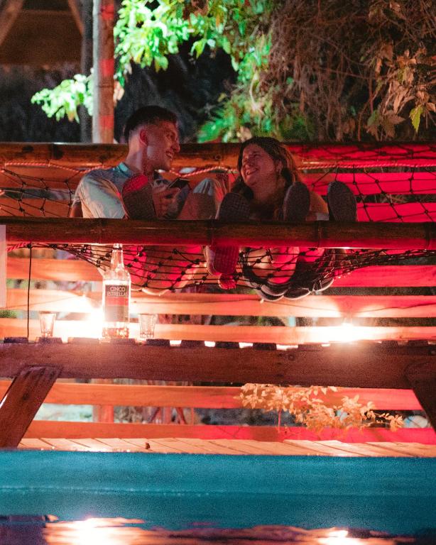 a man and woman sitting on a bench at a pool at El Zoo Hostel, Bar & Pool in Palomino