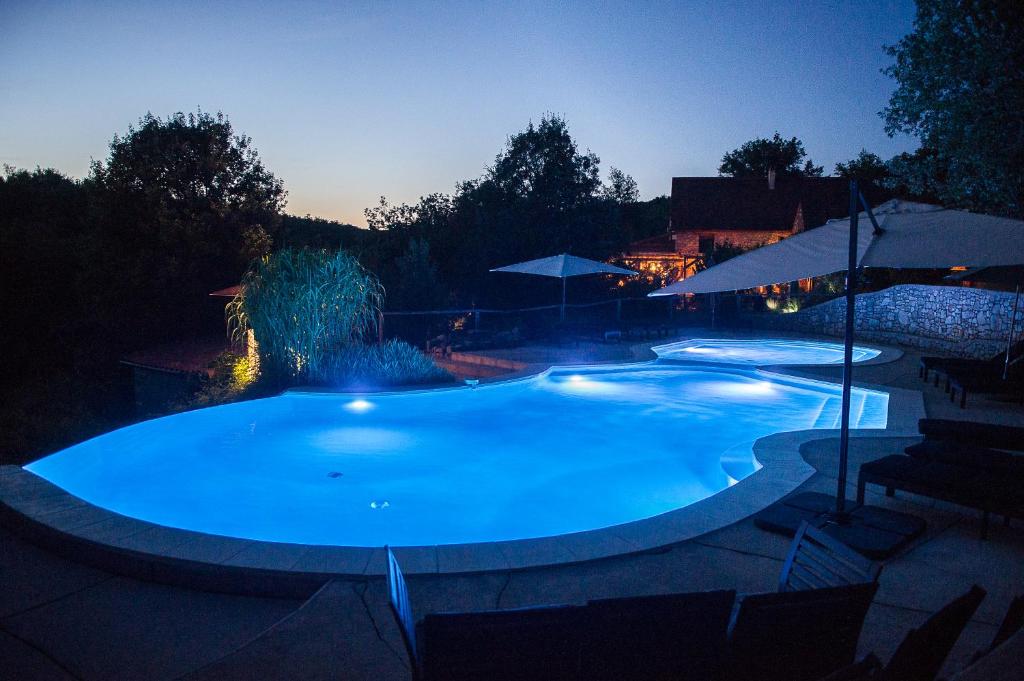 Aux Lodges du Mas de Nadal في Sauliac-sur-Célé: حمام سباحة كبير في الليل مع أضواء