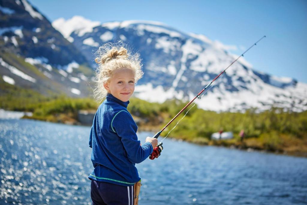 a little girl holding a fishing pole in front of a lake at Signegarden - Midt i fjellheimen - Tett på Fjord-Norge in Skjåk