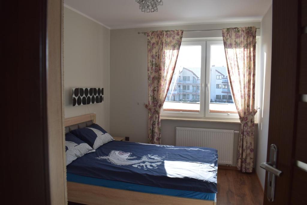 ein Schlafzimmer mit einem Bett mit blauer Decke und einem Fenster in der Unterkunft Apartament Deluxe in Darłówko