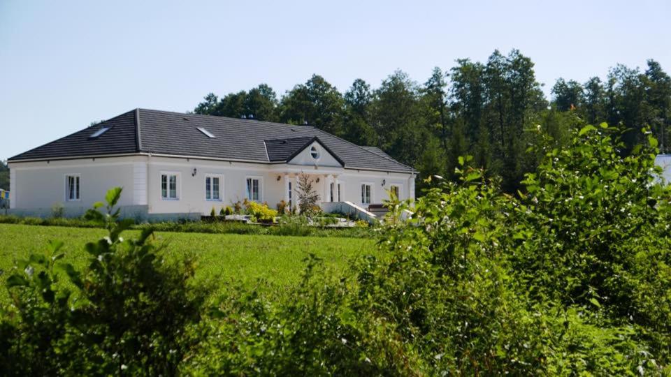 a white house with a black roof in a field at Olszynowy Dwór in Zwola Poduchowna