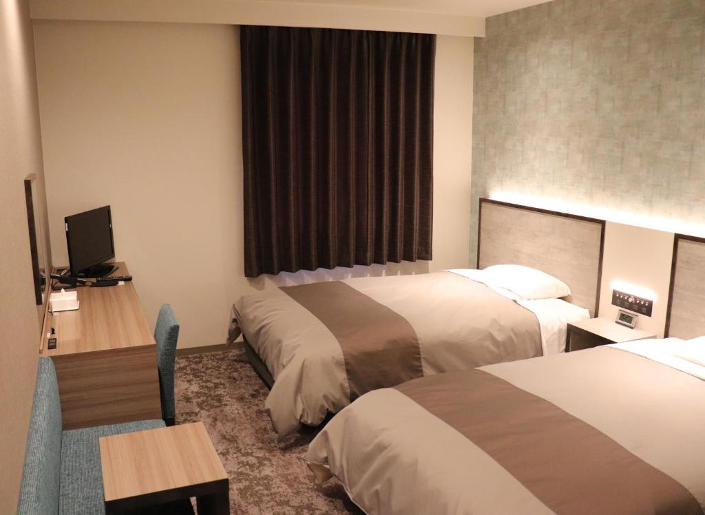 高知市にあるツーリストイン高知のベッド2台とデスクが備わるホテルルームです。