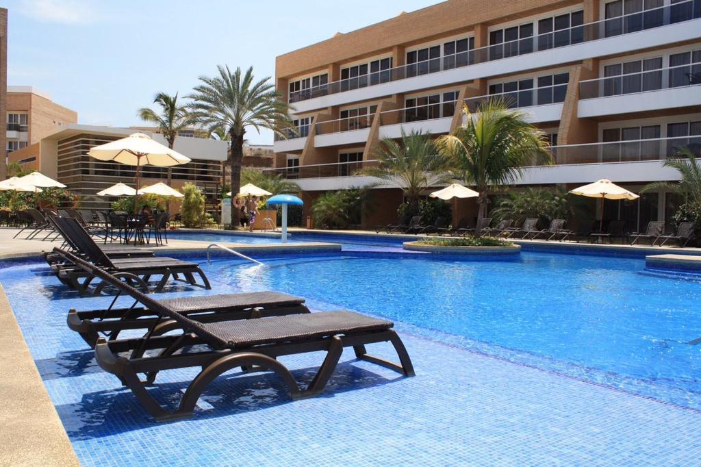 uma piscina com cadeiras e guarda-sóis ao lado de um hotel em Hotel Margarita Real em Pampatar