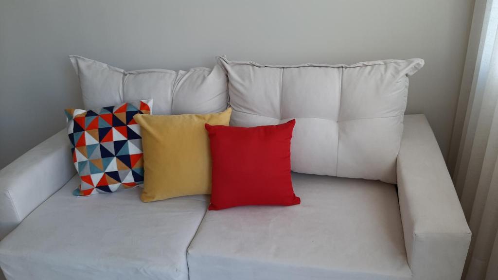 Un sofá blanco con tres almohadas de colores. en Mix aparts -Apartamento perfeito em Tijucas -SC en Tijucas