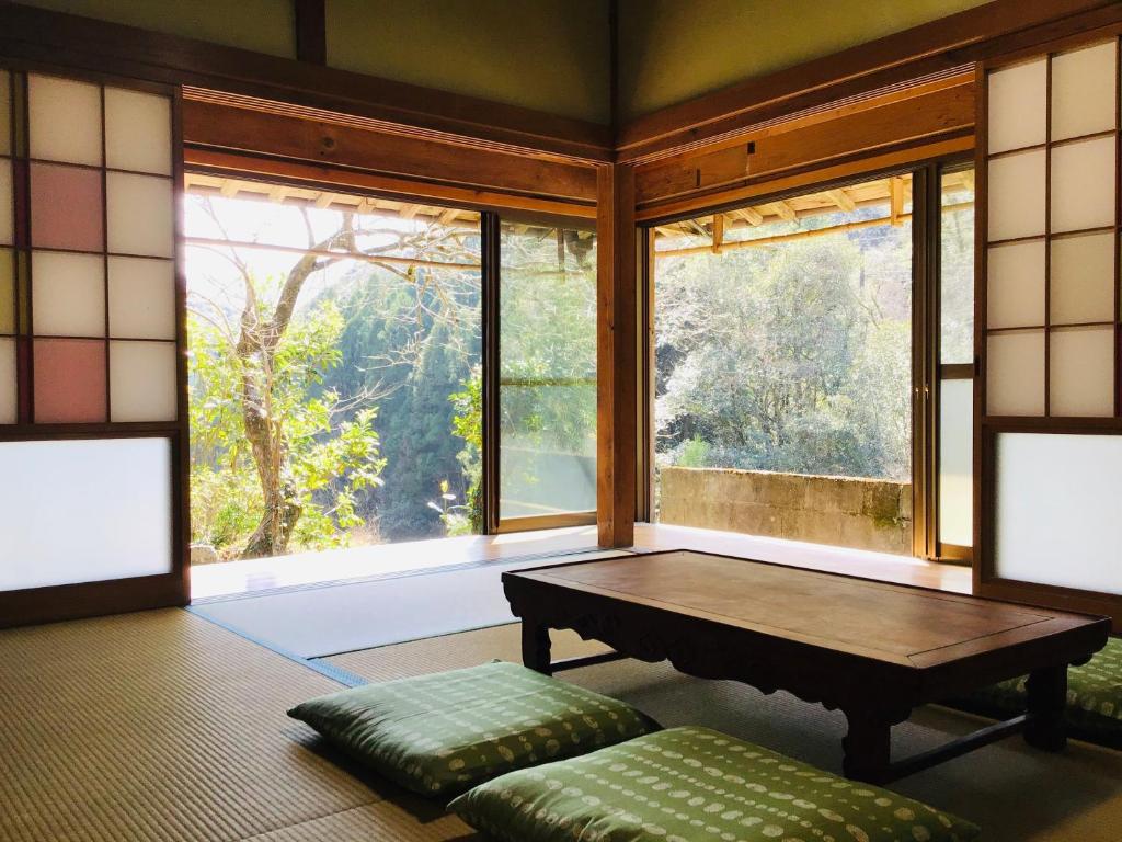 a room with a table and a bench and windows at 古民家宿　寝つきいいキツネ in Shimanto