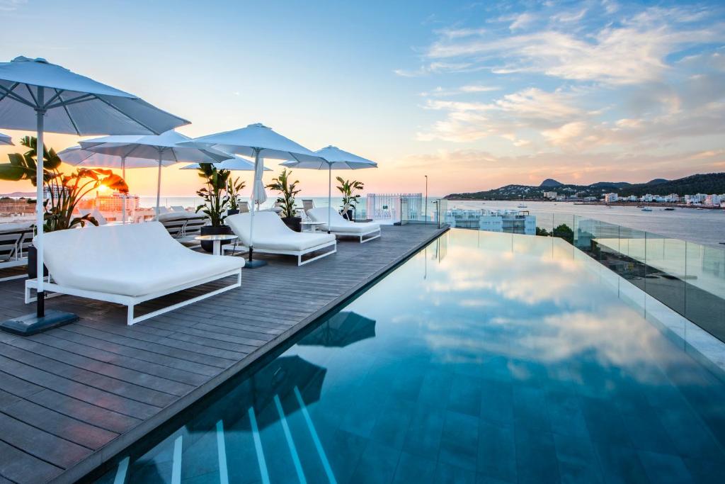 ein Pool mit Stühlen und Sonnenschirmen auf einem Gebäude in der Unterkunft INNSiDE by Meliá Ibiza Beach in Bucht von San Antonio