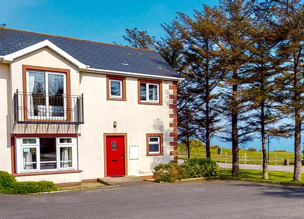 a white house with a red door and trees at Seacliff HH No 8 in Dunmore East