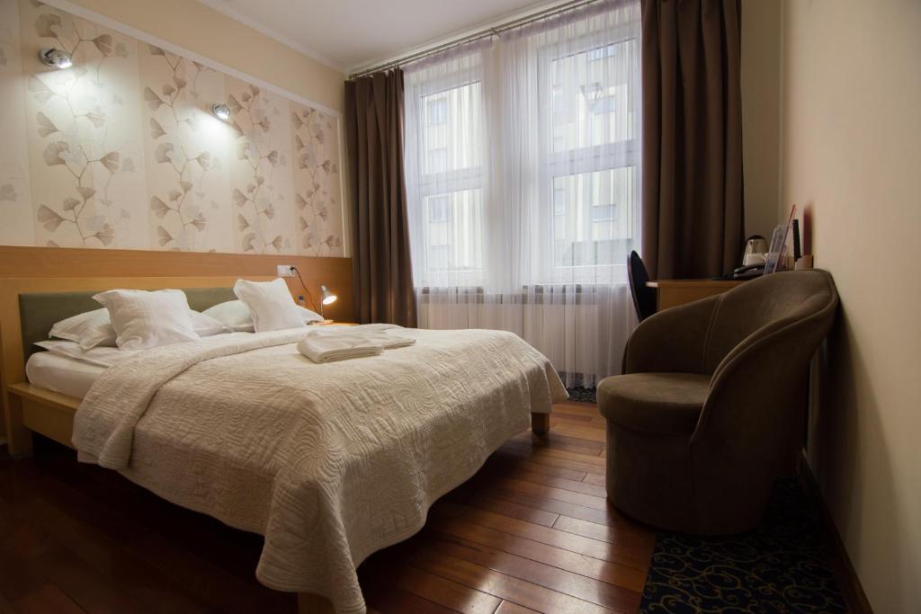 a bedroom with a bed and a chair and a window at Hotel Trojka in Przemyśl