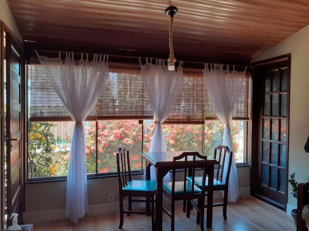 ein Esszimmer mit Tisch und Stühlen und Fenstern in der Unterkunft Linda casa Rio das Ostras, ar condicionado, wifi, churrasqueira e garagem in Rio das Ostras