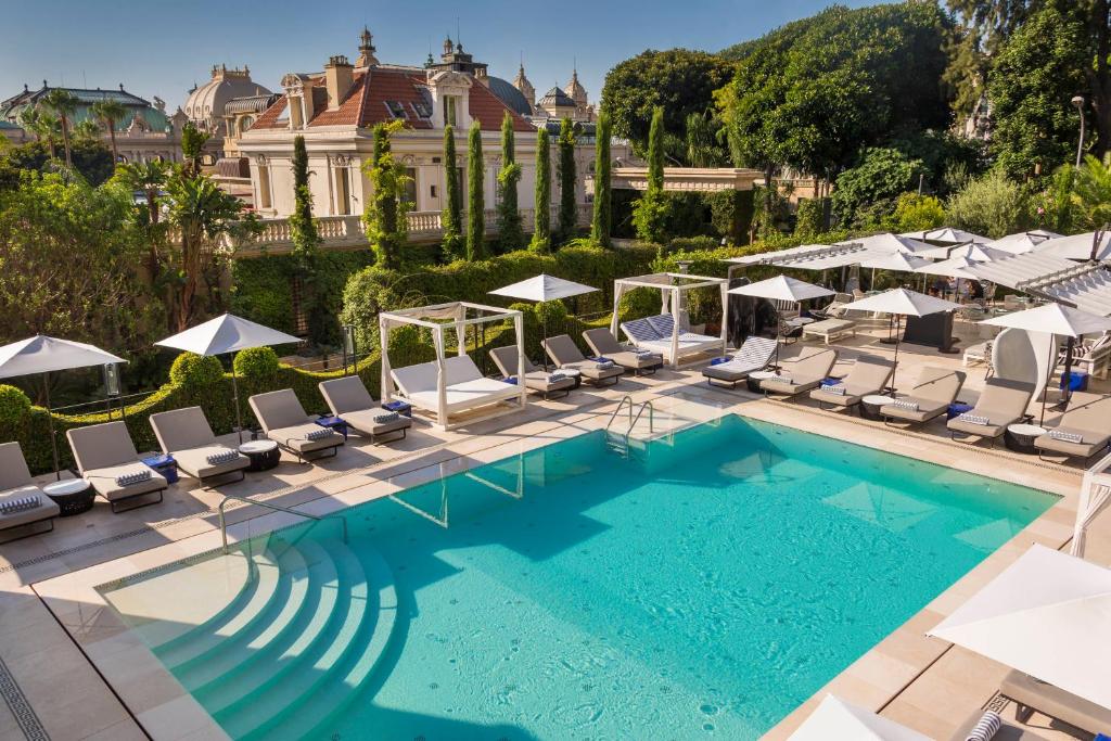 una piscina con sedie a sdraio e un edificio di Hôtel Métropole Monte-Carlo - Deux restaurants étoilés a Monte Carlo