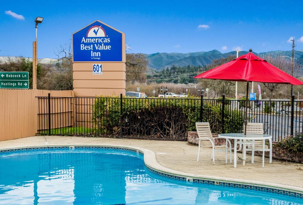 a pool with a table and a red umbrella at Americas Best Value Inn - Ukiah in Ukiah