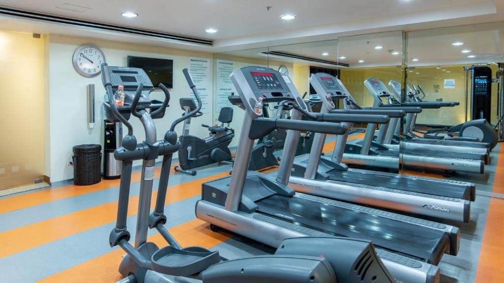 A compact cardio gym with treadmills, ellipticals, and a wall clock.