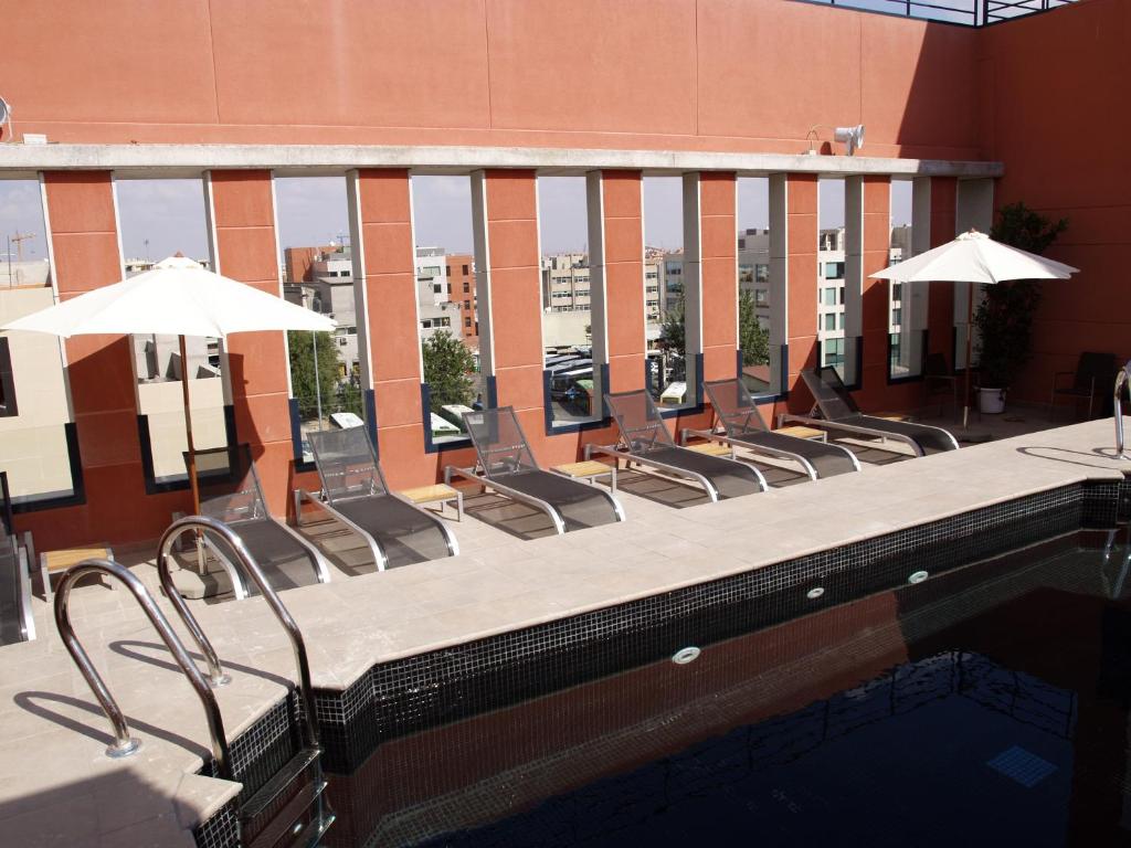 une piscine avec des chaises et des parasols dans un bâtiment dans l'établissement Eco Alcalá Suites, à Madrid