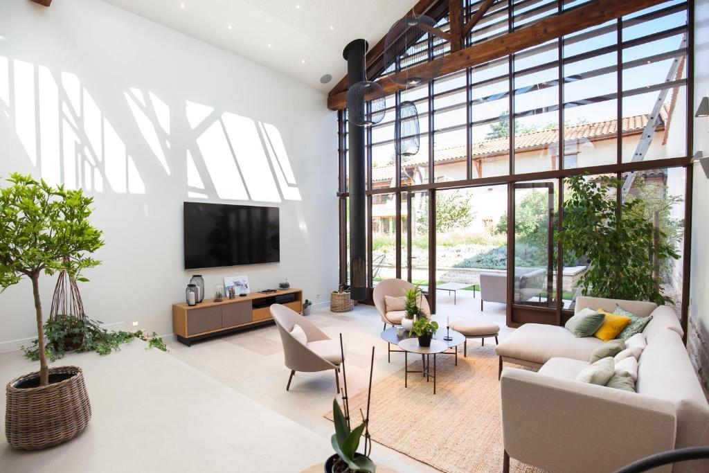 uma sala de estar com mobiliário branco e janelas grandes em Le Relais de la Godasse em Reyrieux
