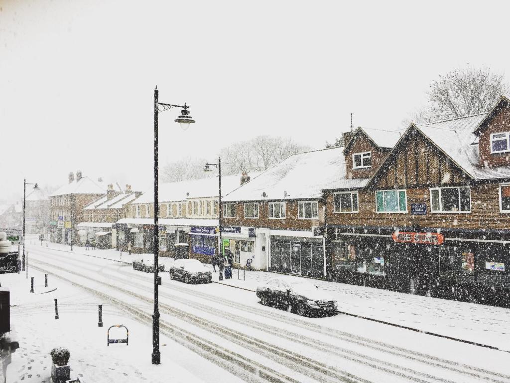 a snow covered street with buildings and cars on it at Cheam Village Self Contained Flat & studio in Cheam