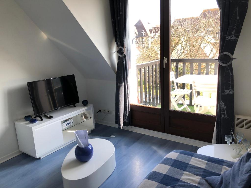 a living room with a television and a balcony at Appartement Cabourg bord de mer in Cabourg