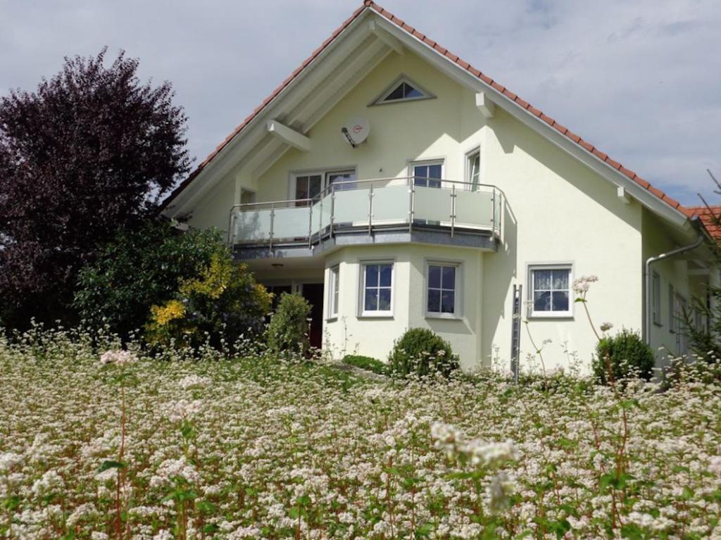 a white house with a balcony in a field of flowers at Ferienwohnung Vogelsang in Herdwangen-Schönach