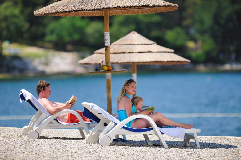 a family sitting on the beach under an umbrella at Valamar Diamant Hotel in Poreč
