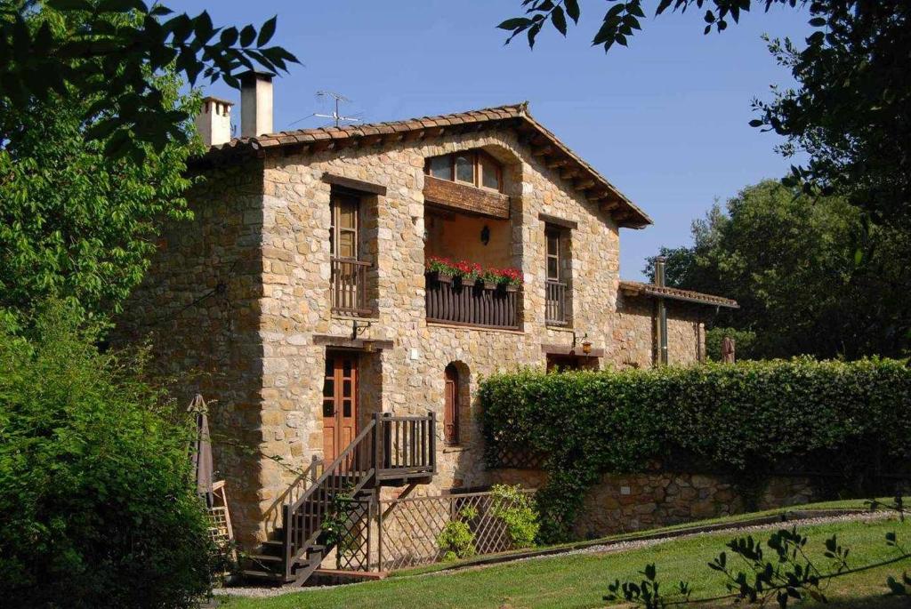 Casa de piedra antigua con balcón y flores en Can Cruanyes, en Sales del Llierca