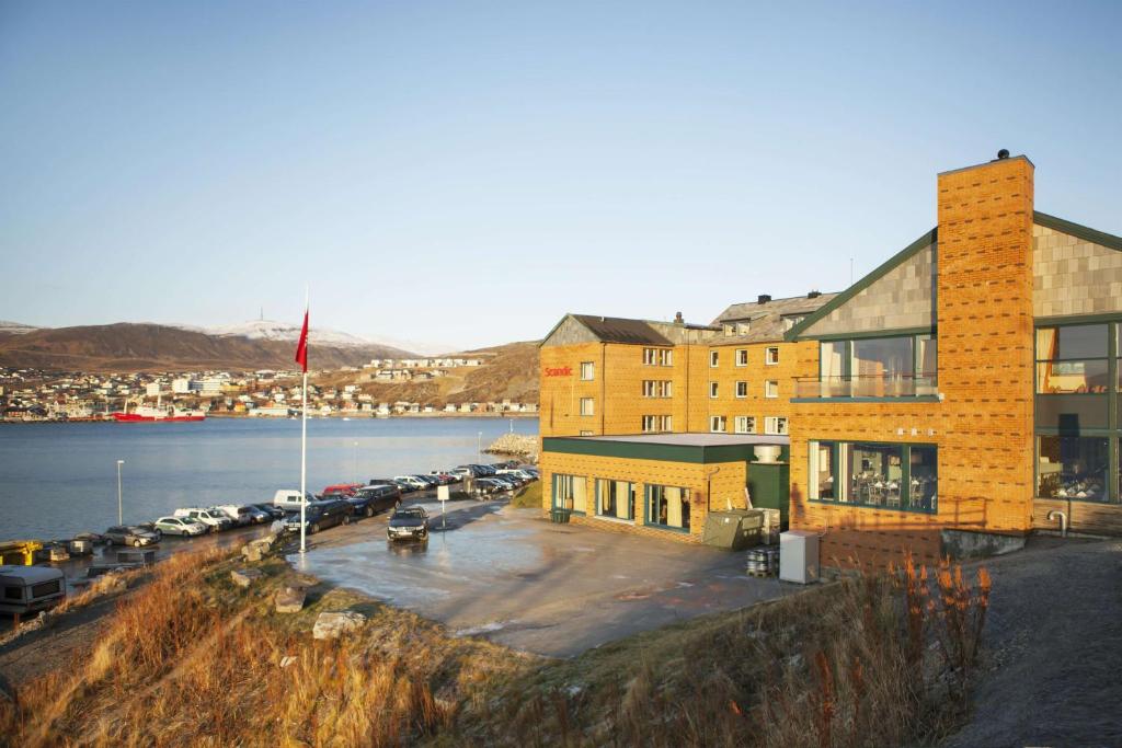 a building with a parking lot next to a body of water at Scandic Hammerfest in Hammerfest