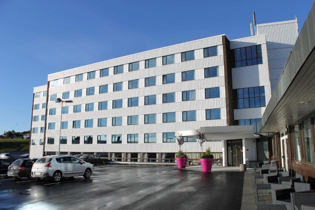 un gran edificio blanco con coches aparcados en un aparcamiento en Frichs Hotel Hamar, en Hamar