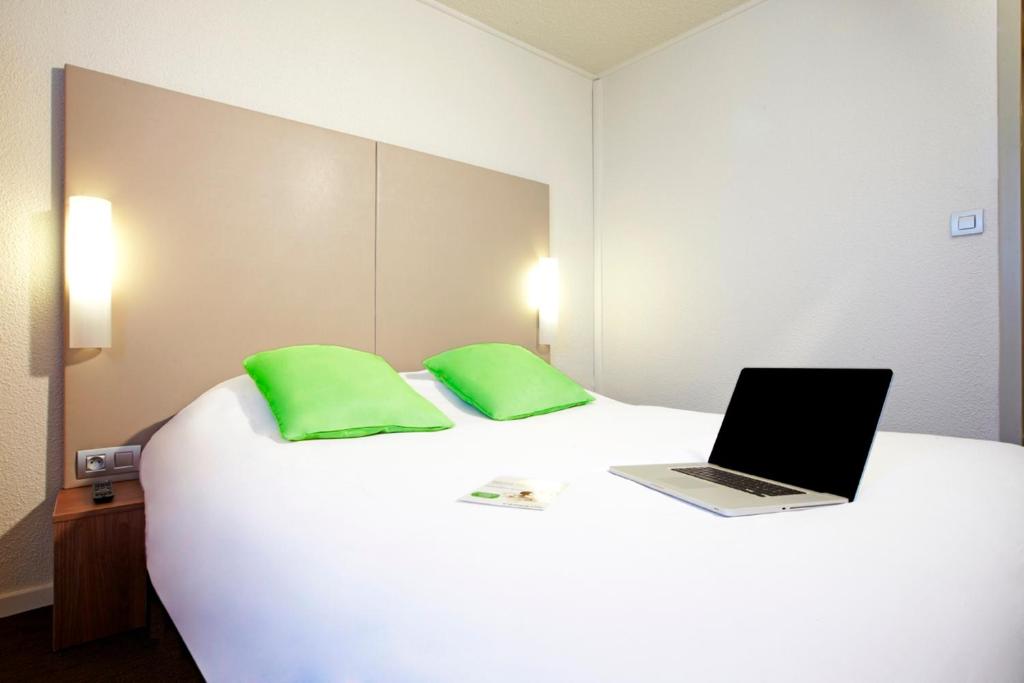 a bed with a laptop on it with two green pillows at Campanile Paris Est Bobigny in Bobigny
