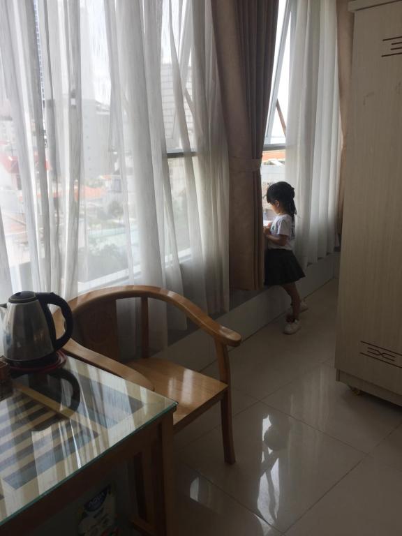 a little girl sitting in a chair looking out of a window at Khách Sạn Flower Sky Nha Trang in Nha Trang