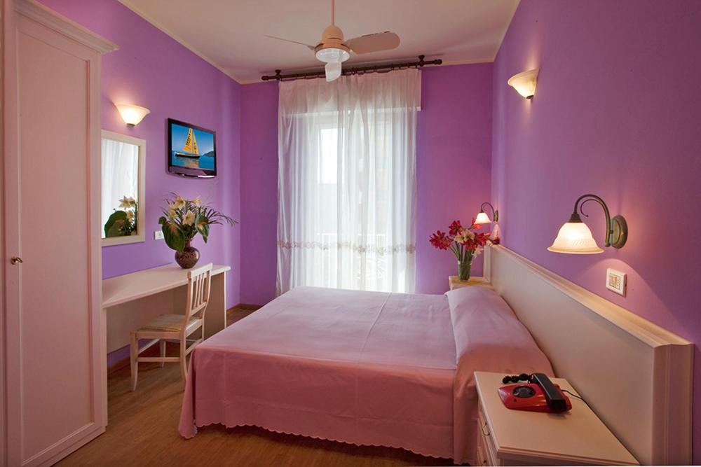 Dormitorio púrpura con cama y escritorio en Hotel Plaza, en Gabicce Mare