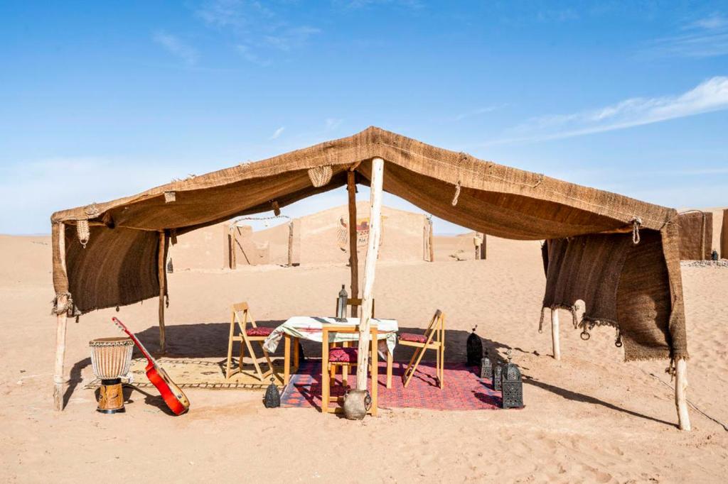 a tent in the desert with a table and chairs at Berber Camp & Desert Tours in Mhamid