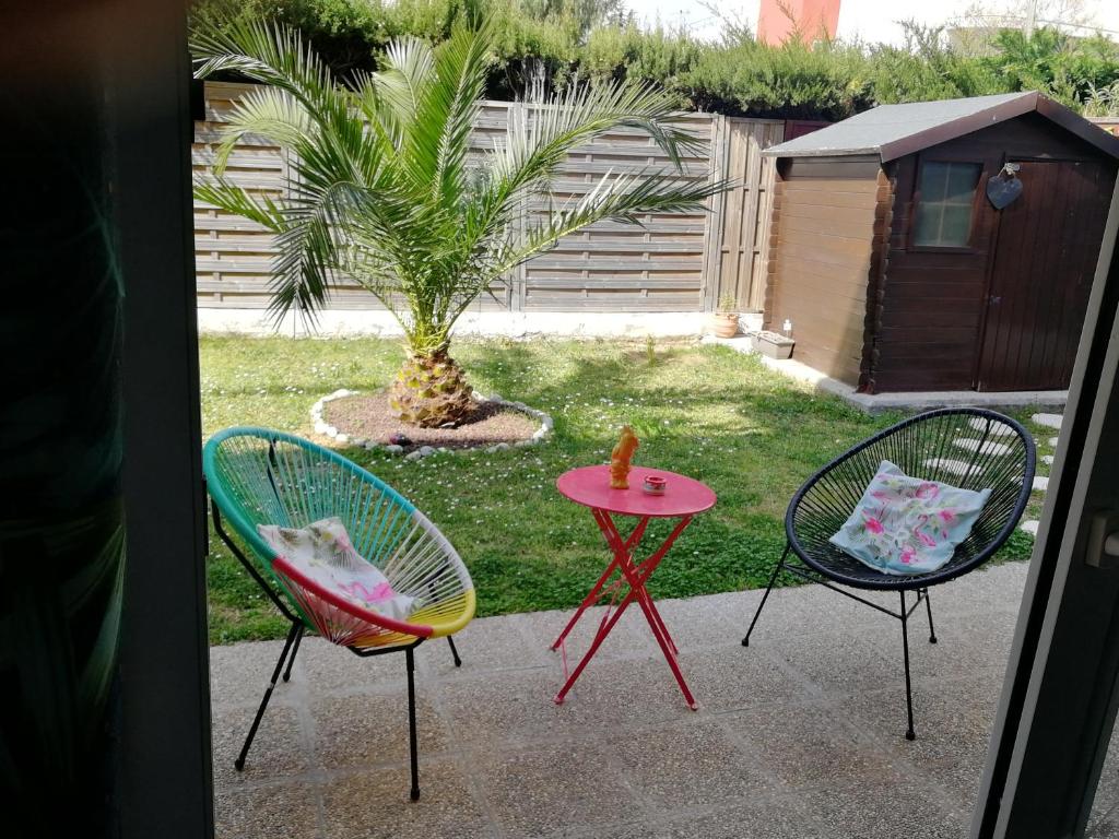 3 Stühle und ein Tisch im Garten mit einer Palme in der Unterkunft Lovely Studio & Garden - près des plages Cagnes-sur-Mer in Cagnes-sur-Mer