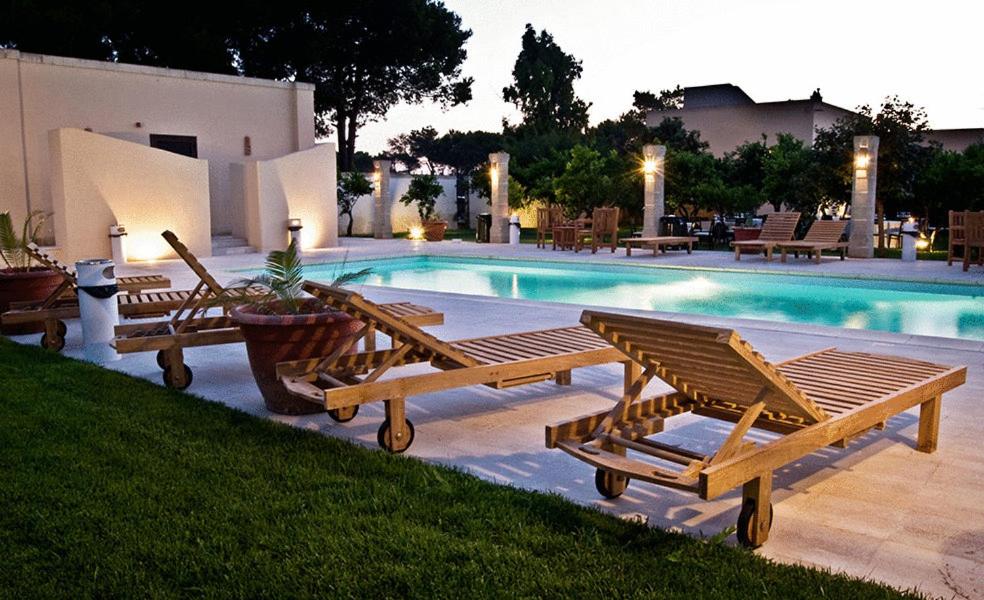 a group of wooden benches next to a swimming pool at Masseria Li Campi in Cavallino di Lecce