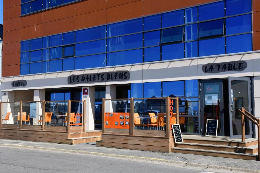 ein Restaurant mit orangefarbenen Stühlen vor einem Gebäude in der Unterkunft Hotel Les Galets Bleus in Cayeux-sur-Mer