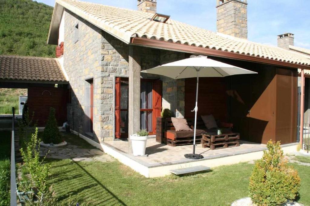 una piccola casa in pietra con ombrellone e sedia di Casa Rural Biescas en el Pirineo a Gavín