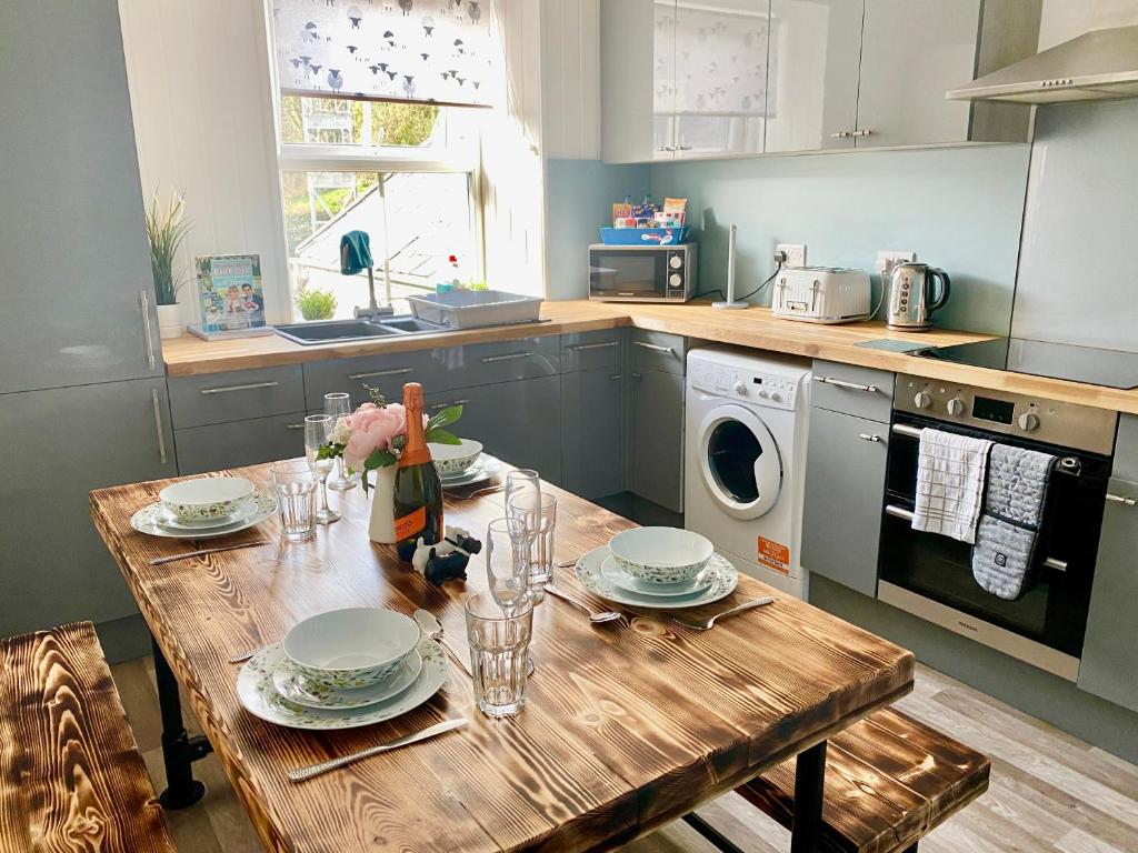 a kitchen with a wooden table with plates and glasses at Hiraeth Môn in Menai Bridge