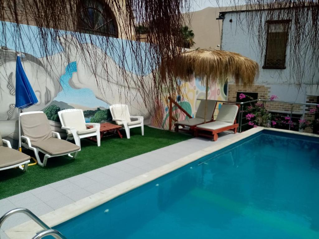 a swimming pool with chairs and a wall with a mural at Hostal Huacachina Sunset in Ica