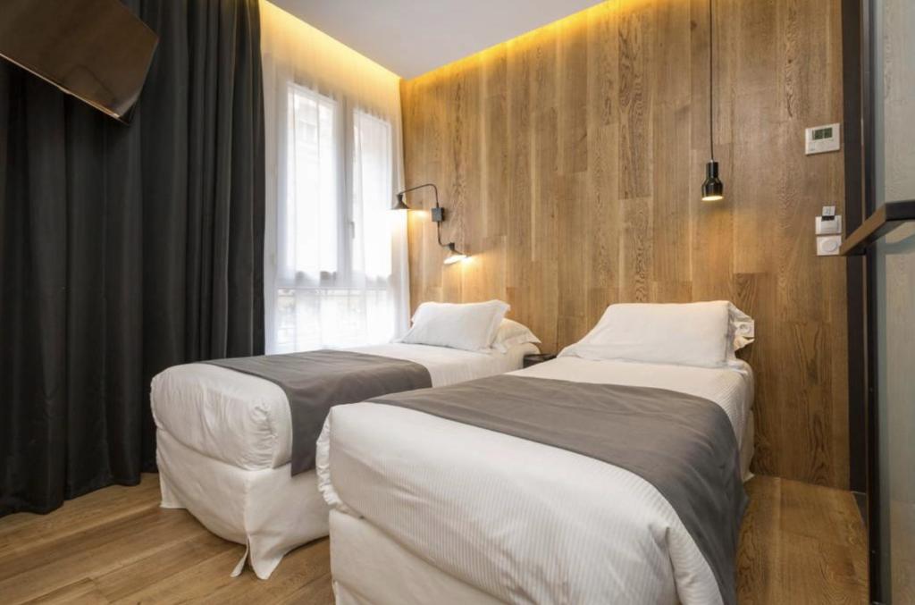 two beds in a room with wooden walls at Atypik Hotel in Clichy