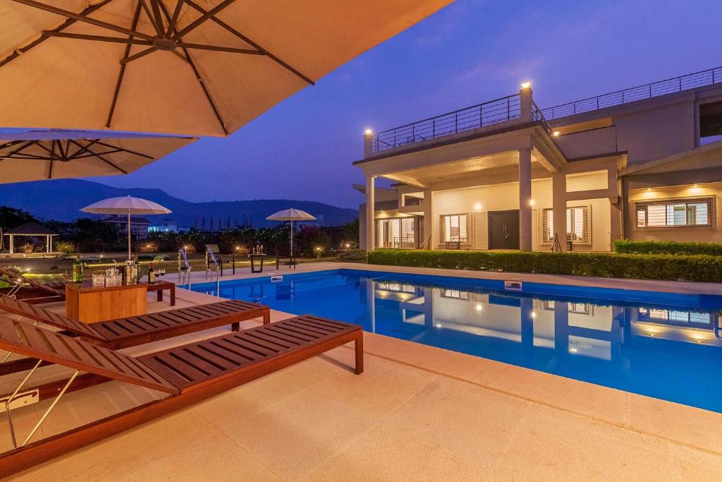 a house with a swimming pool with chairs and an umbrella at Casa Del Vento by StayVista - Villa showcasing a swimming pool, Terrace with deck & A lush lawn with a gazebo for a delightful stay in Lonavala