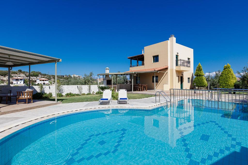 a swimming pool with two chairs in front of a house at Dina & Pelagia Villas, Serene Country Escapes, By ThinkVilla in Roumelí