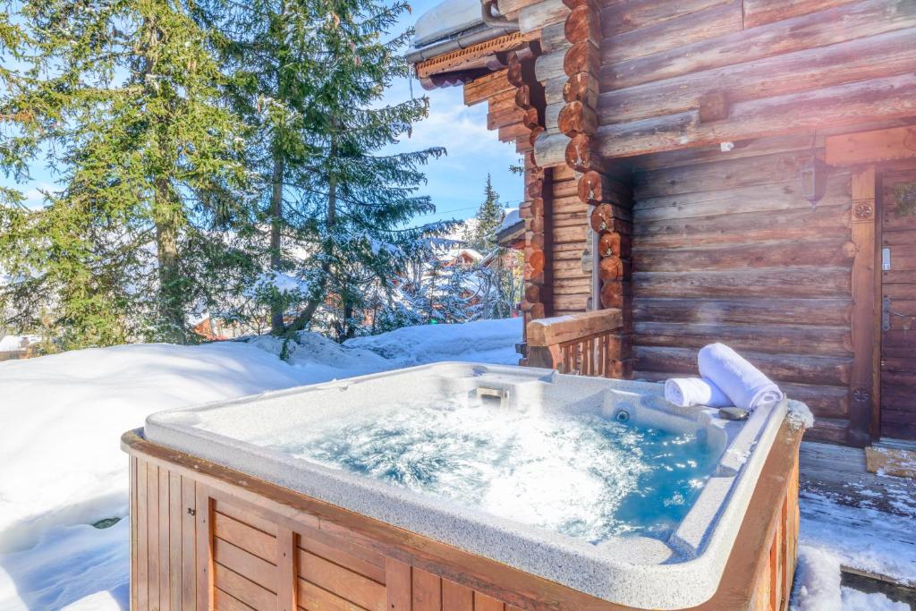 a hot tub outside of a log cabin in the snow at Madame Vacances Chalet Elliot Ouest in La Tania