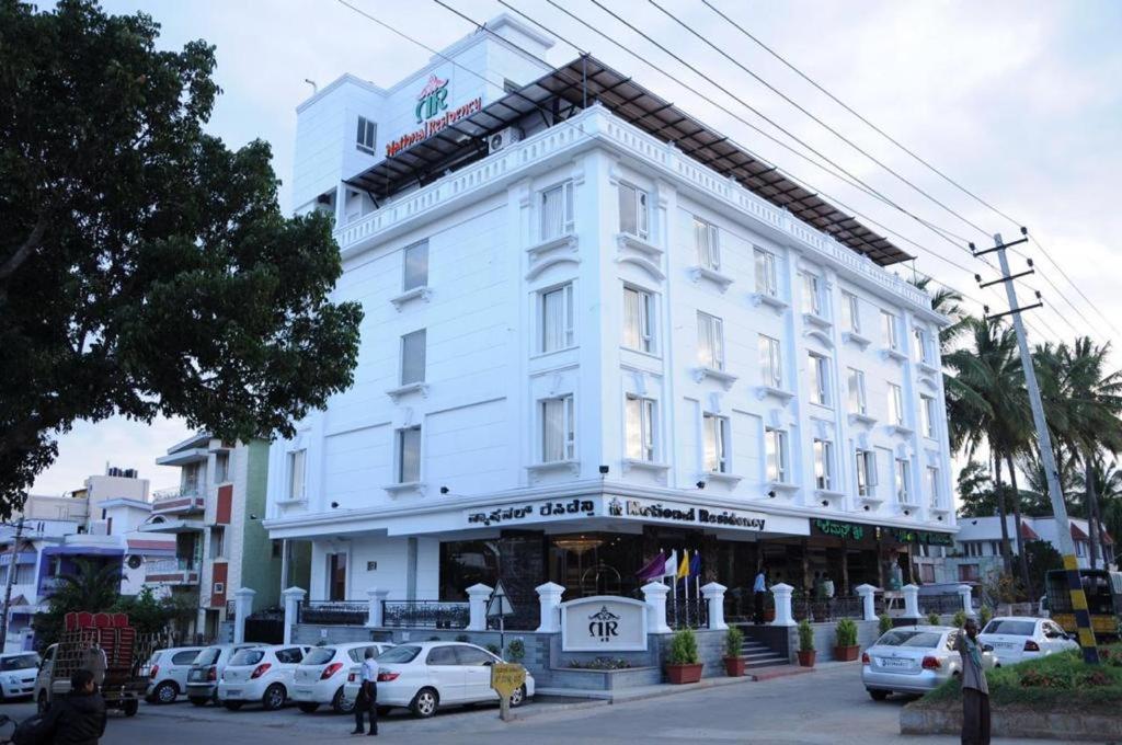 un edificio blanco con coches estacionados frente a él en National Residency, en Mysore